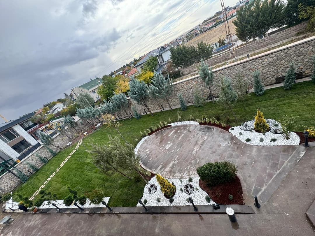 Kendi uygulamamız — geniş villa bahçesinde dairesel oturma alanı, çim ve bitki kuşaklarıyla tamamlanmış peyzaj